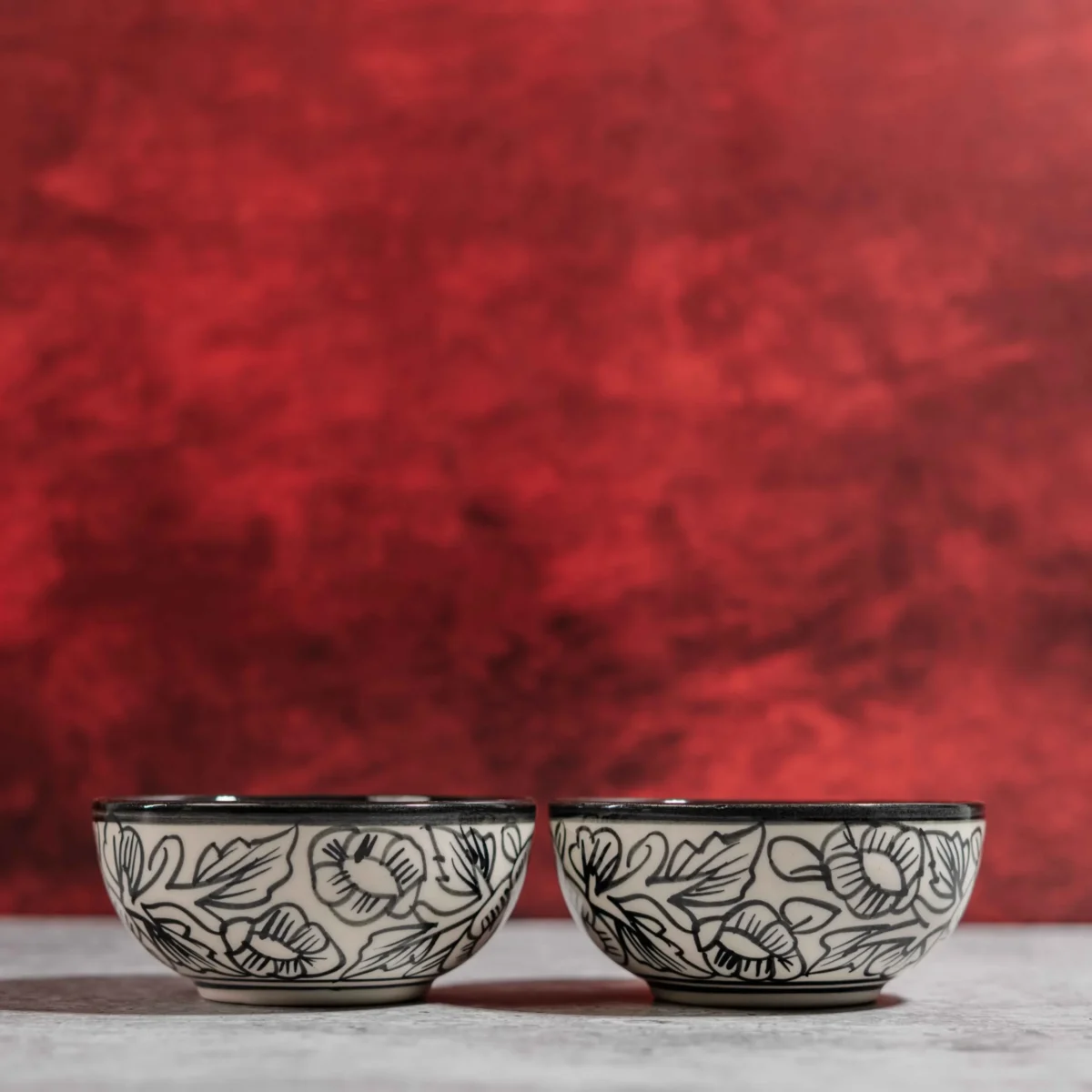 Monarca Ceramic Katori Bowls – Set of 2 by Harmiche. Hand-painted black floral design, microwave & dishwasher safe. Perfect for curries, dal & desserts.